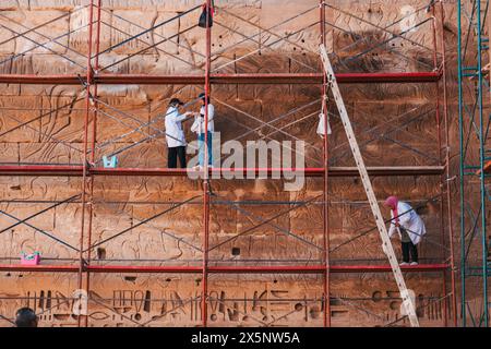 Des ouvriers en blouse de laboratoire sur échafaudage travaillent à restaurer et à préserver les murs de pierre du temple à Medinet Habu à Louxor, en Égypte Banque D'Images