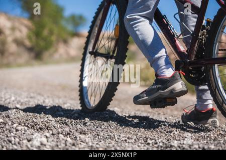 Une personne sur un vélo se tient debout avec son pied sur le sol sur une route rocheuse. La personne porte des baskets et des chaussettes. Banque D'Images