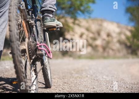 Une personne fait du vélo avec ses pieds sur les pédales. Le vélo est sur un chemin de terre avec une colline rocheuse en arrière-plan. Banque D'Images