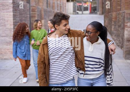 Couple de sexes divers étudiants heureux qui se promènent dans les bras sur le campus de l'université Banque D'Images