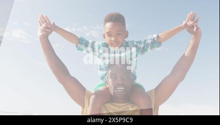 Père afro-américain soulevant son fils sur les épaules, tous deux souriant sous ciel dégagé Banque D'Images