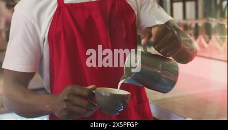 Un jeune professionnel afro-américain versant du lait dans une tasse à café Banque D'Images