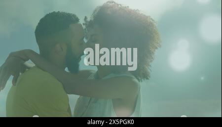 Image de taches de lumière contre un couple afro-américain s'embrassant l'un l'autre Banque D'Images