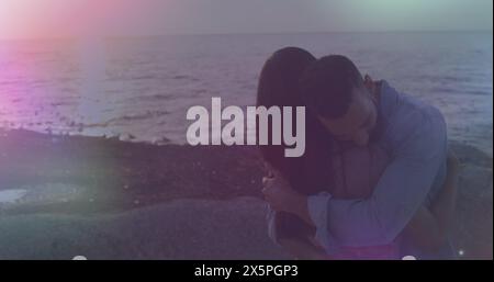 Image de taches de lumière contre un couple afro-américain s'embrassant à la plage Banque D'Images