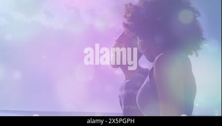 Image de taches de lumière contre un couple afro-américain marchant ensemble à la plage Banque D'Images