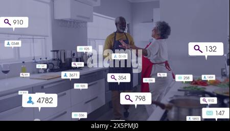 Image de barres de notification sur couple afro-américain senior avec tablier dansant dans la cuisine Banque D'Images