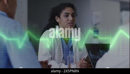 Image d'un moniteur de fréquence cardiaque contre un médecin biracial discutant avec son équipe à l'hôpital Banque D'Images