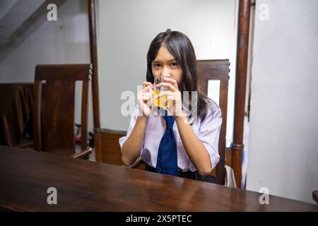 Portrait d'une lycéenne asiatique dans un petit déjeuner uniforme avec boire du jus d'orange le matin avant de se préparer pour l'école Banque D'Images