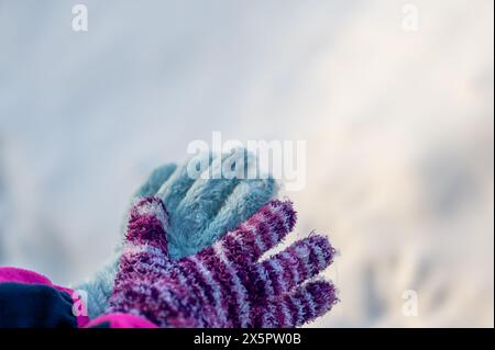 Une paire de gants non assortis sur un enfant tenu sur un fond de neige blanc Banque D'Images