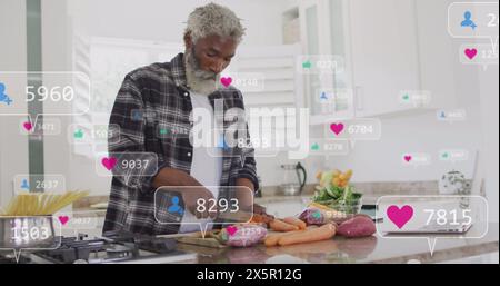 Image de barres de notification sur un homme afro-américain senior coupant des légumes dans la cuisine à la maison Banque D'Images