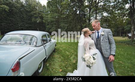 Mariée et mariée posant devant la voiture blanche pour l'image de mariage Banque D'Images