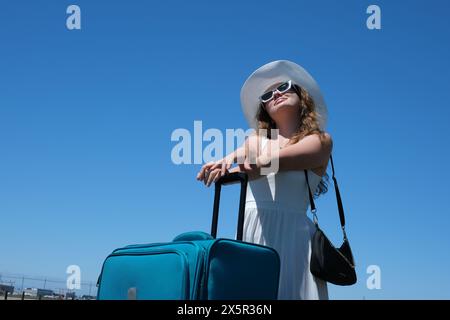 Gros plan jambes de femme marche sur la route asphaltée et le monde de voyage avec la valise de voyage. Les femmes font de l'auto-stop dans le pays. Une jeune fille dans une robe blanche et un énorme chapeau avec valise voyage autour du globe Banque D'Images