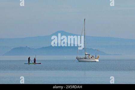 Portobello, Édimbourg, Écosse, Royaume-Uni. 11 mai 2024. Matin brumeux à 14 degrés centigrades pour ceux qui sortent pour exrcise sur la plage et le Firth of Forth. Sur la photo : planches de paddle et yacht de plaisance amarré sur Firth of Forth avec une île brumeuse d'Inchkeith et Lomond Hills en arrière-plan. Credit : Arch White/Alamy Live news. Banque D'Images