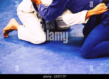 Deux hommes sur un tapis bleu dans un centre d'entraînement du Jiu-Jitsu brésilien. Il est concentré et pratique les techniques de l'art martial Banque D'Images