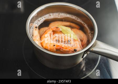 Les crevettes sont bouillies dans de l'eau dans une casserole en acier inoxydable sur une plaque à induction. Les crevettes rouges fraîches sont bouillies avec des feuilles de laurier. Foyer sélectionné. Haute qualité Banque D'Images