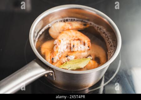 Les grosses crevettes sont bouillies dans de l'eau avec des feuilles de laurier. Une casserole sur une plaque de cuisson à induction avec des crevettes royales bouillies. Foyer sélectionné. Photo de haute qualité Banque D'Images