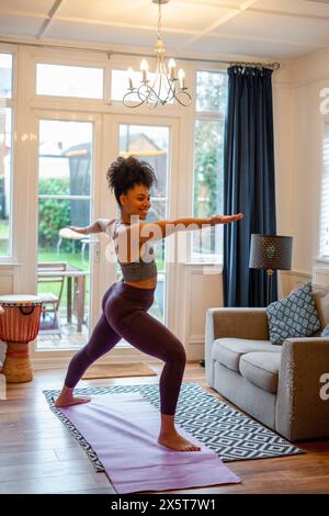 Jeune femme souriante faisant du yoga à la maison Banque D'Images