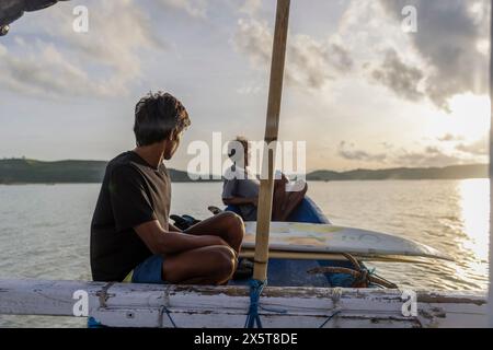 Indonésie, Lombok, Surfers regardant la vue sur la mer depuis le bateau au coucher du soleil Banque D'Images
