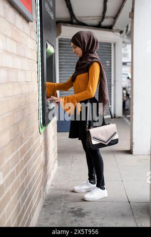 Femme en hijab utilisant ATM Banque D'Images