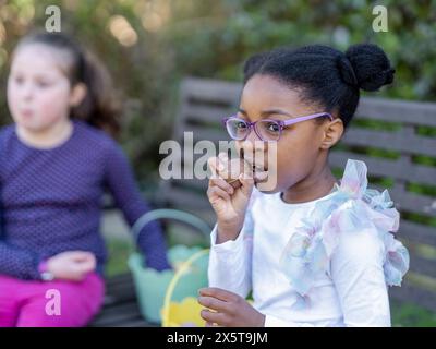 Filles amies (6-7) mangeant des œufs de chocolat de Pâques Banque D'Images