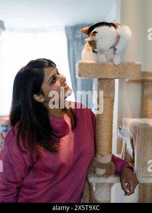 Portrait de femme regardant le chat assis sur le poteau à gratter à la maison Banque D'Images