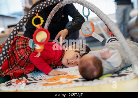 Soeurs (4-5, 0-1 mois) jouant sur un tapis de jouet, père en arrière-plan Banque D'Images