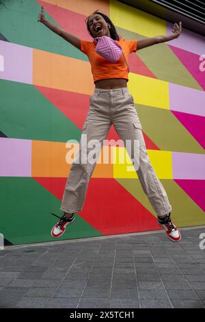 Jeune femme souriante sautant contre un mur coloré Banque D'Images