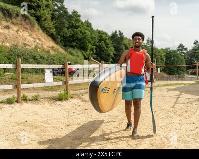 Jeune homme portant paddleboard et rame sur la plage Banque D'Images