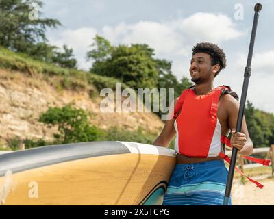 Jeune homme portant paddleboard et rame sur la plage Banque D'Images