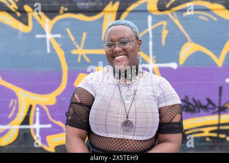 Portrait d'une personne non binaire souriante contre un mur de graffiti Banque D'Images