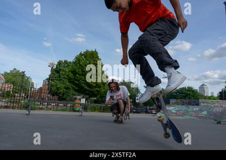 Homme enregistrant un ami faisant des tours de skateboard Banque D'Images