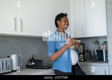 Femme enceinte souriante tenant une assiette avec des raisins rouges dans la cuisine Banque D'Images