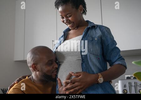 Homme embrassant le ventre d'une femme enceinte dans la cuisine Banque D'Images