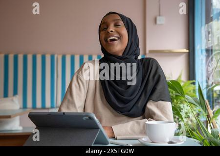 Jeune femme souriante en hijab travaillant sur tablette dans un café Banque D'Images