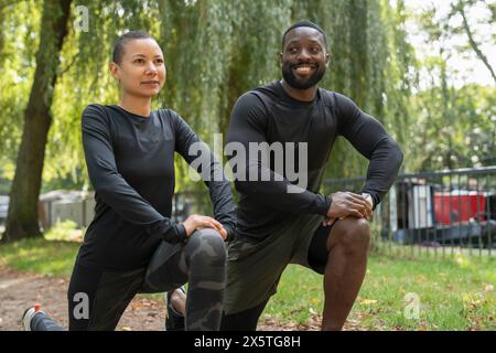 Homme souriant et femme étirant les jambes dans le parc Banque D'Images