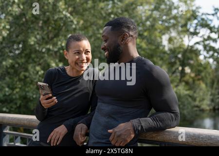 Homme sportif souriant et femme tenant un téléphone intelligent dans le parc Banque D'Images