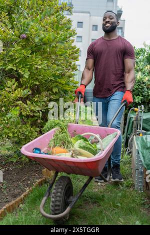 Portrait d'homme souriant avec des légumes dans la brouette dans le jardin urbain Banque D'Images