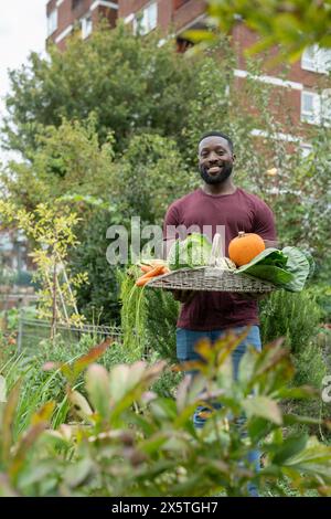 Portrait de l'homme souriant tenant panier avec des légumes frais dans le jardin urbain Banque D'Images