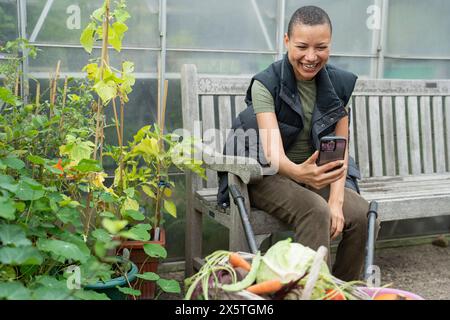 Femme souriante photographiant des légumes récoltés avec un téléphone intelligent Banque D'Images