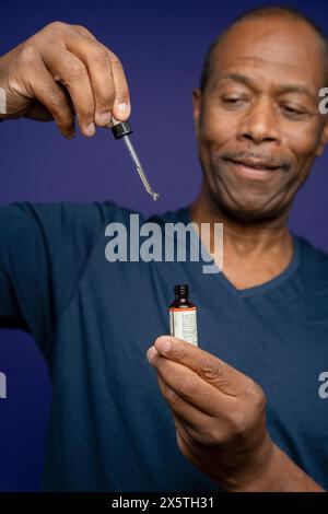 Portrait de l'homme prenant la médecine avec pipette sur fond violet Banque D'Images