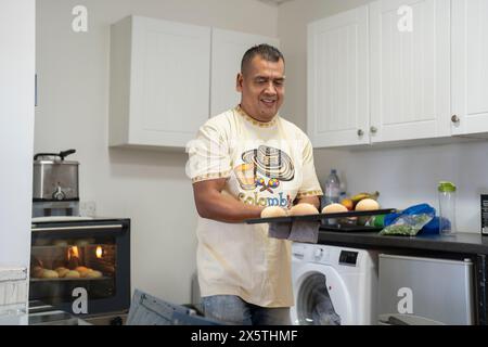 Homme tenant un plateau de petits pains fraîchement cuits dans la cuisine Banque D'Images