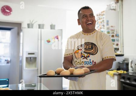 Homme tenant un plateau de petits pains fraîchement cuits dans la cuisine Banque D'Images