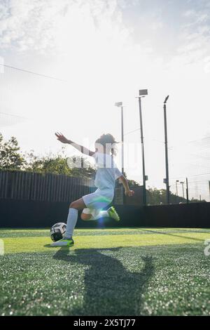 Fille (6-7) jouant au football sur le terrain de football Banque D'Images