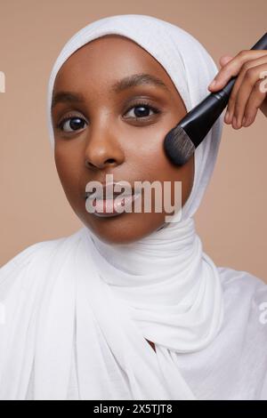 Portrait studio d'une jeune femme en hijab blanc appliquant le maquillage Banque D'Images