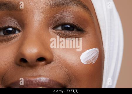 Portrait studio d'une jeune femme en hijab blanc appliquant la crème pour le visage Banque D'Images