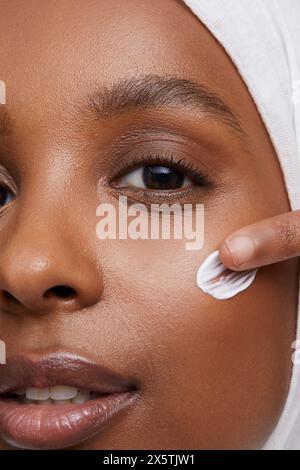 Portrait studio d'une jeune femme en hijab blanc appliquant la crème pour le visage Banque D'Images