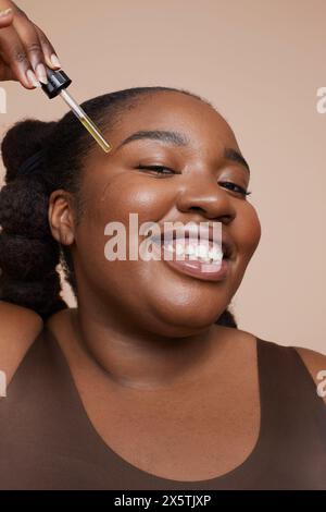 Photo studio d'une jeune femme souriante appliquant un sérum pour le visage Banque D'Images