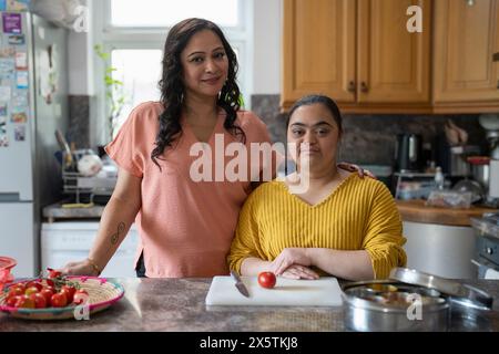 Portrait d'une mère avec une fille trisomique du syndrome de Down préparant la nourriture en cuisine Banque D'Images