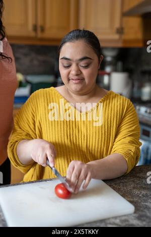 Jeune femme atteinte du syndrome de Down coupant la tomate en cuisine Banque D'Images