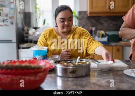 Jeune femme trisomique préparant la nourriture en cuisine Banque D'Images